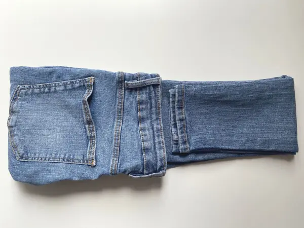 Klappe ein Hosenbein über das andere und falte sowohl den Hosenbund als auch die Beine bis fast zur Mitte um. Achte darauf noch einen kleinen Spalt freizulassen. Klappe ein Hosenbein über das andere und falte sowohl den Hosenbund als auch die Beine bis fast zur Mitte um. Achte darauf noch einen kleinen Spalt freizulassen.