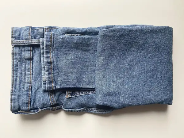 Falte deine Jeans einmal zur Mitte hoch und im Anschluss ein zweites Mal, um ein kleines Päckchen zu erhalten. Falte deine Jeans einmal zur Mitte hoch und im Anschluss ein zweites Mal, um ein kleines Päckchen zu erhalten.