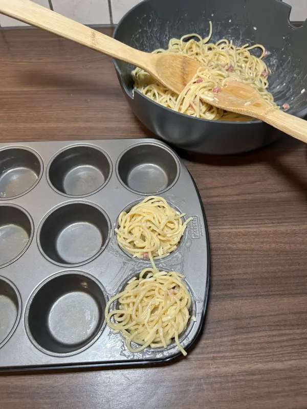 Verteile die Spaghettimischung jetzt auf die zwölf Muffinförmchen. Nimm dabei nur wenige Nudeln zwischen das Salatbesteck, so geht es einfacher. Außerdem kleckerst du so auch weniger. Verteile die Spaghettimischung jetzt auf die zwölf Muffinförmchen. Nimm dabei nur wenige Nudeln zwischen das Salatbesteck, sonst werden die Förmchen zu voll. Außerdem kleckerst du so auch weniger.