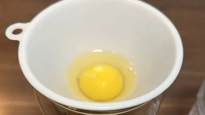 Schlage ein Ei an der Kante des Glases ohne Trichter auf. Kippe nun den Eiinhalt in den Trichter. Jetzt fließt das Eiklar aus dem Trichter unten heraus. Das Eigelb ist aber ein bisschen zu dick und passt nicht durch. Perfekt! Denn nur das brauchen wir für unser Rezept. Schlage ein Ei an der Kante des Glases ohne Trichter auf. Kippe nun den Eiinhalt in den Trichter. Jetzt fließt das Eiklar aus dem Trichter unten heraus. Das Eigelb ist aber ein bisschen zu dick und passt nicht durch. Perfekt! Denn nur das brauchen wir für unser Rezept.