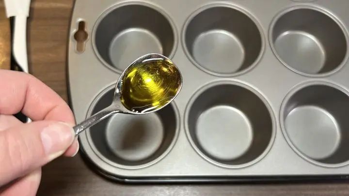 Mit einem kleinen Teelöffel und Olivenöl kannst du deine Muffinform ganz leicht einfetten. Gib einfach etwas Öl auf den kleinen Löffel, damit es nicht zu viel wird. Langsam tröpfelst du dann in jedes Förmchen etwas Öl hinein. Bereite Deine Muffinform für köstliche Spaghetti-Muffins vor. Ein wenig Olivenöl auftragen, um ein Ankleben zu verhindern.
