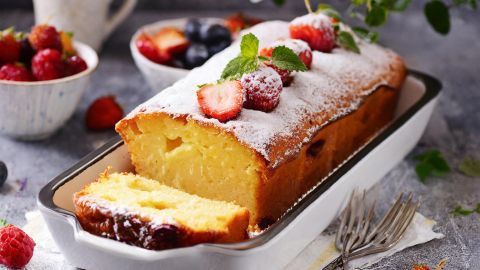 Quarknapfkuchen in Kastenform mit Puderzucker bestreut, dekoriert mit Erdbeeren und Minze, auf einem Tisch mit Beeren.