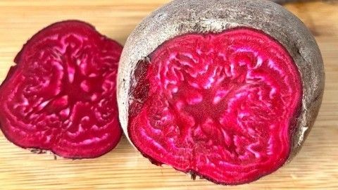 Rote Bete liegt auf einem Holzbrett, ein geschnittener Teil zeigt die brillante, rote Farbe und die interessante Struktur.