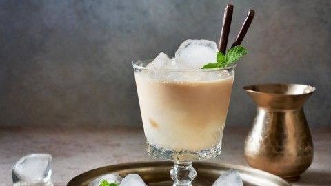 Ein elegantes Getränk im Glas mit Eiswürfeln, garniert mit Minze und Schokoladenstiften auf einem Silbertablett.