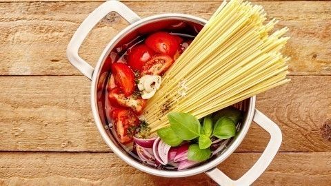 Ein Topf mit frischen Tomaten, Zwiebeln, Basilikum und Spaghetti wird für ein einfaches One-Pot-Gericht vorbereitet.