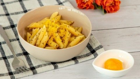 Pasta liegt in einer Schüssel, garniert mit gebeiztem Eigelb, daneben ein gelbes Eigelb in einer kleinen Schale, Blumen im Hintergrund.