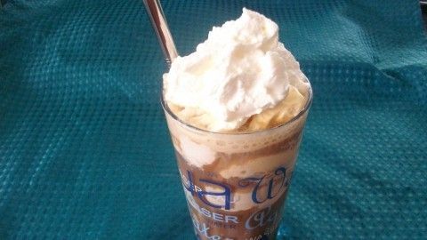 Ein Glas Eiskaffee steht auf einem blauen Hintergrund. Oben darauf befindet sich eine große Haube aus Sahne.