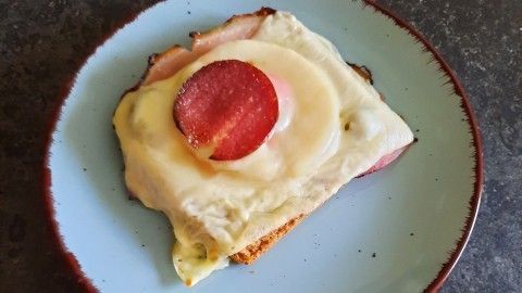 Ein belegter Toast mit Schinken, geschmolzenem Käse und einer Scheibe Ananas liegt auf einem blauen Teller.