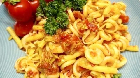 Eine Teller Sommerpasta mit Knoblauch und Tomaten, garniert mit frischem Petersilie und Kirschtomaten, auf einem blauen Teller.