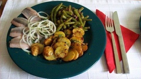 Auf einem türkisfarbenen Teller liegen Herzhafte Matjesfilets mit Röstkartoffeln und Bohnen, garniert mit Zwiebeln.