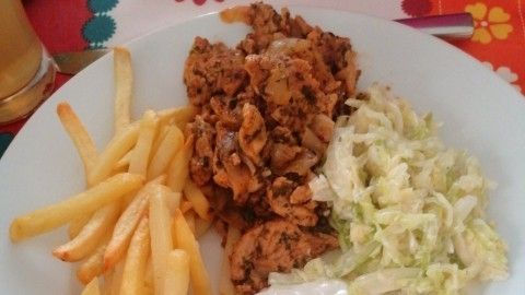 Saftiges Gyros mit Tsatsiki liegt auf einem weißen Teller, umgeben von Pommes und frischem Salat, auf buntem Tisch.