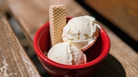 Kugel Zitronen-Buttermilch-Eis liegt in einer roten Schüssel und wird von einer Waffel begleitet, auf einem Holzuntergrund.