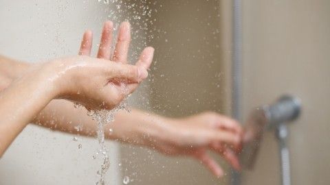 Hände fangen sprudelndes Wasser auf, während der Wasserstrahl aus einer Dusche fließt, in einem Badezimmer-Umfeld.