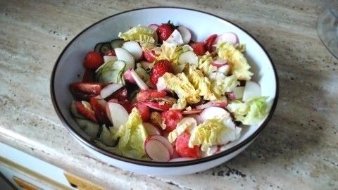 Frischer Salat mit Gemüse und Obst wird in einer Schüssel angerichtet und steht auf einer marmorierten Arbeitsfläche.