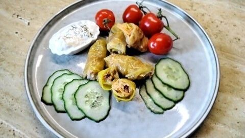 Gefüllter Porree liegt neben frischen Gurkenscheiben auf dem Teller, umgeben von Kirschtomaten und Joghurt Dip.