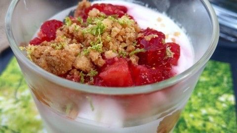 Ein glasiges Erdbeertrifle mit frischen, roten Erdbeeren, knusprigen Bröseln und einer sahnigen Schicht auf grünem Untergrund.