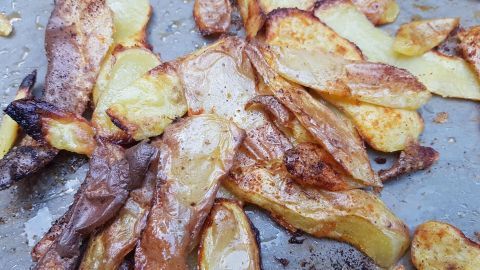 Ein Blech mit knusprig gebackenen Kartoffelschalen liegt auf einem Backblech, umgeben von goldbraunen Kartoffelstücken.