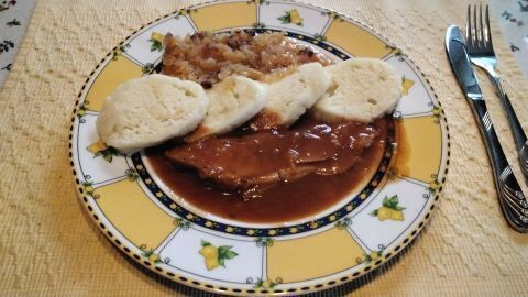 Böhmische Knödel auf einem Teller mit Bratensauce und Sauerkraut, serviert auf gelb gemustertem Geschirr auf einem Tischset.