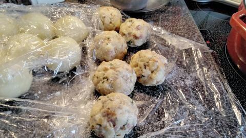 Mehrere handgemachte Böhmische Speckknödel liegen auf Frischhaltefolie, bereit zum Kochen in einer Küchenumgebung.