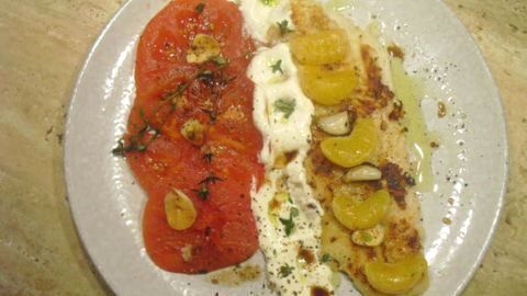 Seelachsfilet mit Creme Fraiche, angerichtet mit Tomatenscheiben und Mandarinen, auf einem weißen Teller am typischen Esstisch.