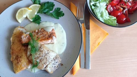 Fischteller mit Dill-Senfsauce serviert mit Zitronenscheiben, Bratkartoffeln und gemischtem Salat auf Holztisch.