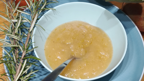 Apfelmus mit Rosmarin in einer Schale auf blauem Teller, daneben frische Äpfel und ein Rosmarinzweig auf Holztisch.