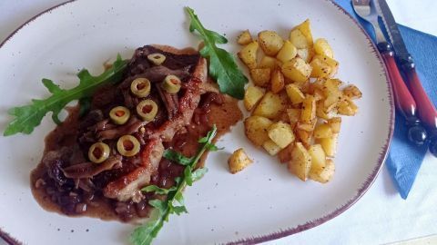 Rumpsteak Mirabeau mit Oliven, Sardellen und Soße auf einem Teller angerichtet.