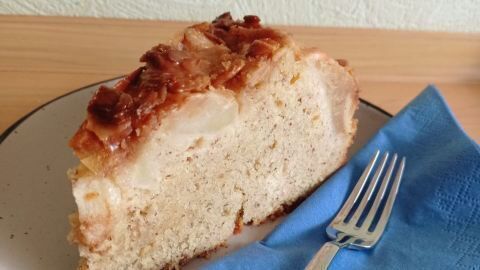 Ein Stück saftiger Apfelkuchen liegt auf einem Teller mit blauem Serviettendekor, daneben liegt eine Gabel.