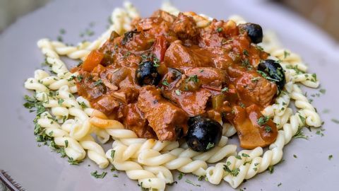 Pasta serviert mit saftiger Pute, Tomatensoße und schwarzen Oliven auf einem Teller, garniert mit Petersilie.