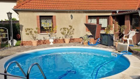 Ein runder Pool mit klarem Wasser steht vor einem Haus, umgeben von bunten Herbstlaub und einer Terrasse mit Gartenmöbeln.