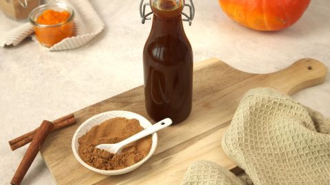 Selbstgemachtes Pumpkin Spice Gewürz und Sirup auf einem Holzbrett, umgeben von einem Kürbis.