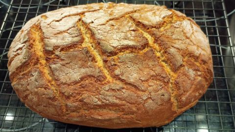 Ein frisch gebackenes Mischbrot mit knuspriger Kruste kühlt auf einem Gitterrost in einer Küche ab.