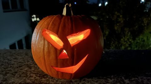 Ein geschnitzter Kürbis leuchtet auf einer Steinmauer in der Dunkelheit, passend zu Halloween, mit einem grinsenden Gesicht.