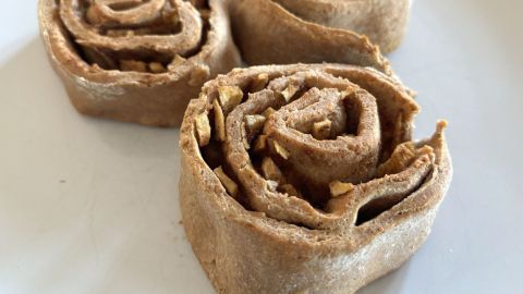 Drei Apfel-Zimt-Schnecken liegen auf einem weißen Teller. Sie sind spiralförmig aufgerollt und gleichmäßig gebacken.