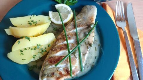 Zanderfilet mit Kräutersoße und Kartoffeln auf blauem Teller, garniert mit Zitrone und Petersilie.