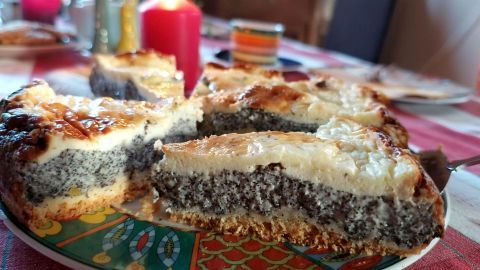 Ein saftiger Mohnkuchen mit Schmand liegt angeschnitten auf einem Tisch mit Kerzenlicht und buntem Geschirr im Hintergrund.