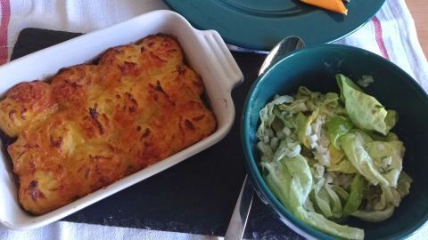 Ein gebackener Cottage Pie in einer weißen Auflaufform neben einer Schüssel Salat.