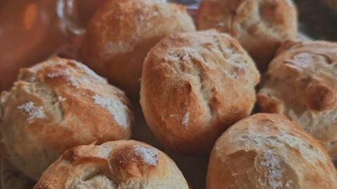 Frische, knusprige Brötchen liegen auf einem Tisch, daneben eine brennende rote Kerze, die eine gemütliche Atmosphäre schafft.