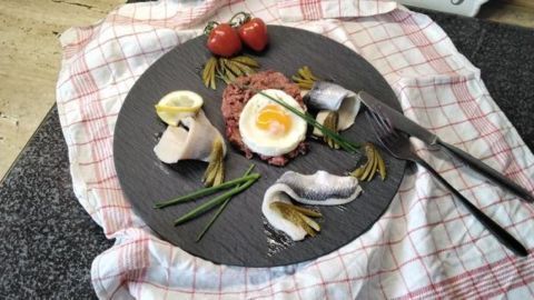 Labskaus: Ein norddeutscher Klassiker mit Corned Beef, Kartoffel und Rote Bete. Mit Matjes, Hering, Gewürzgurken und Spiegelei kunstvoll angerichtet auf Schiefer. Probiere dieses traditionelle Gericht und genieße den besonderen Geschmack.