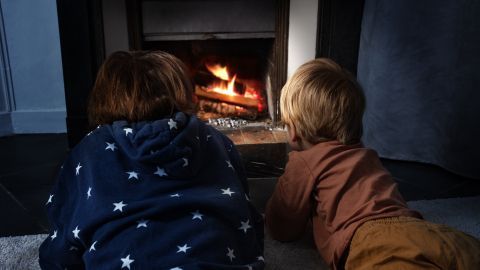 Zwei Kinder liegen gespannt vor dem knisternden Kaminfeuer und lauschen.