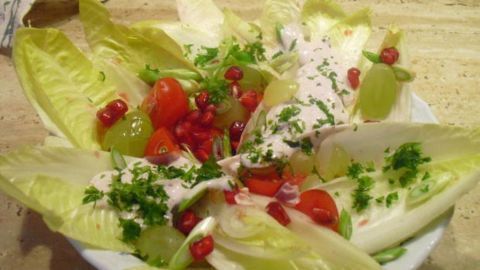 Granatapfelkerne und Chicorée vereint in einem erfrischenden Salat. Dieses visuelle Highlight kombiniert die süßen Noten von Trauben und Granatapfel mit der subtilen Bitterkeit von Chicorée, abgerundet durch frische Kräuter.